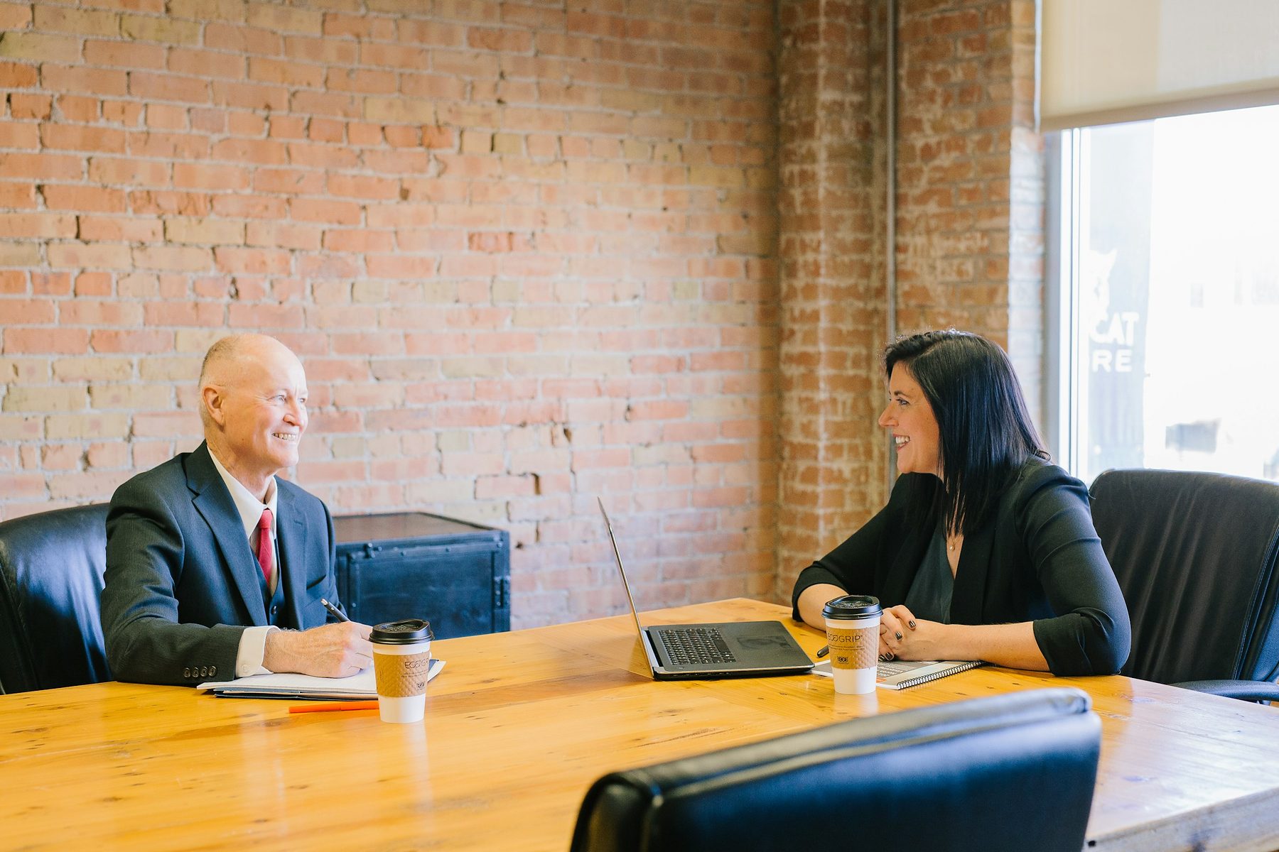 Consultor e cliente conversando à mesa, com anotações e um computador entre os dois